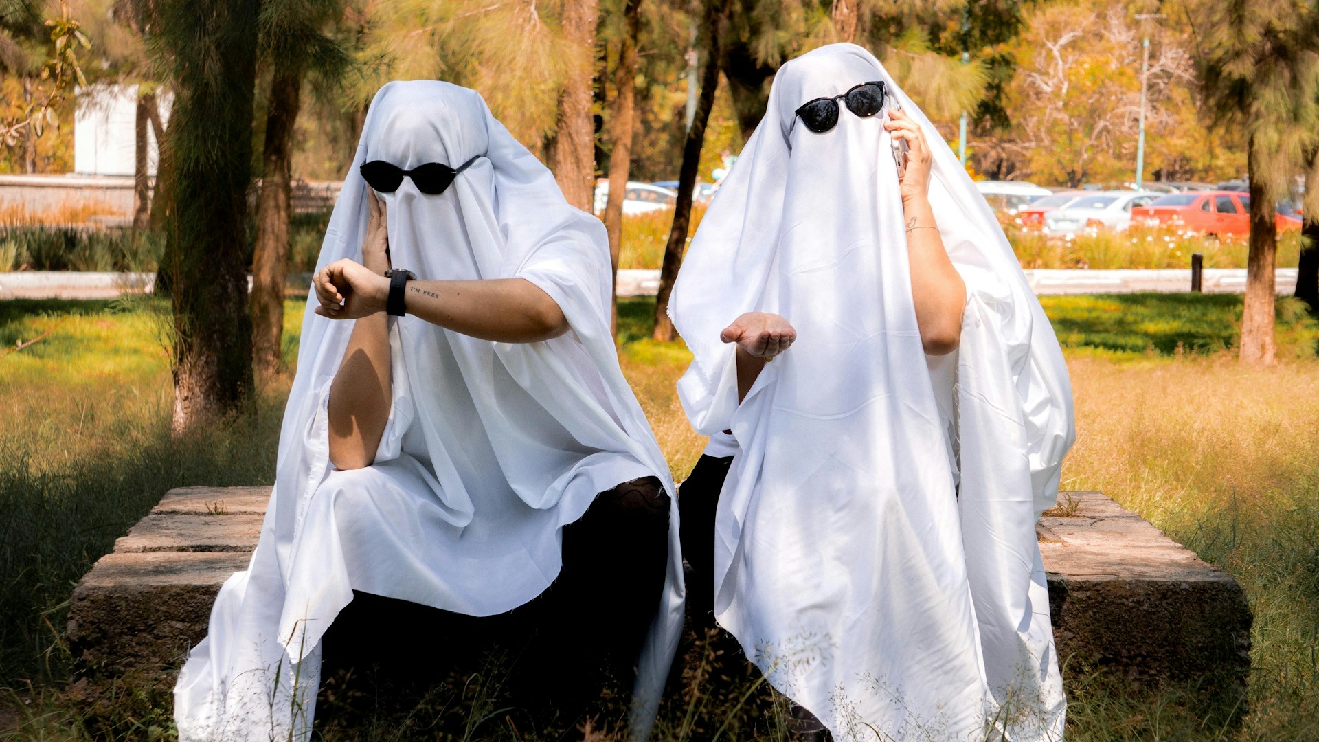 Two people dressed as ghosts sitting outside.