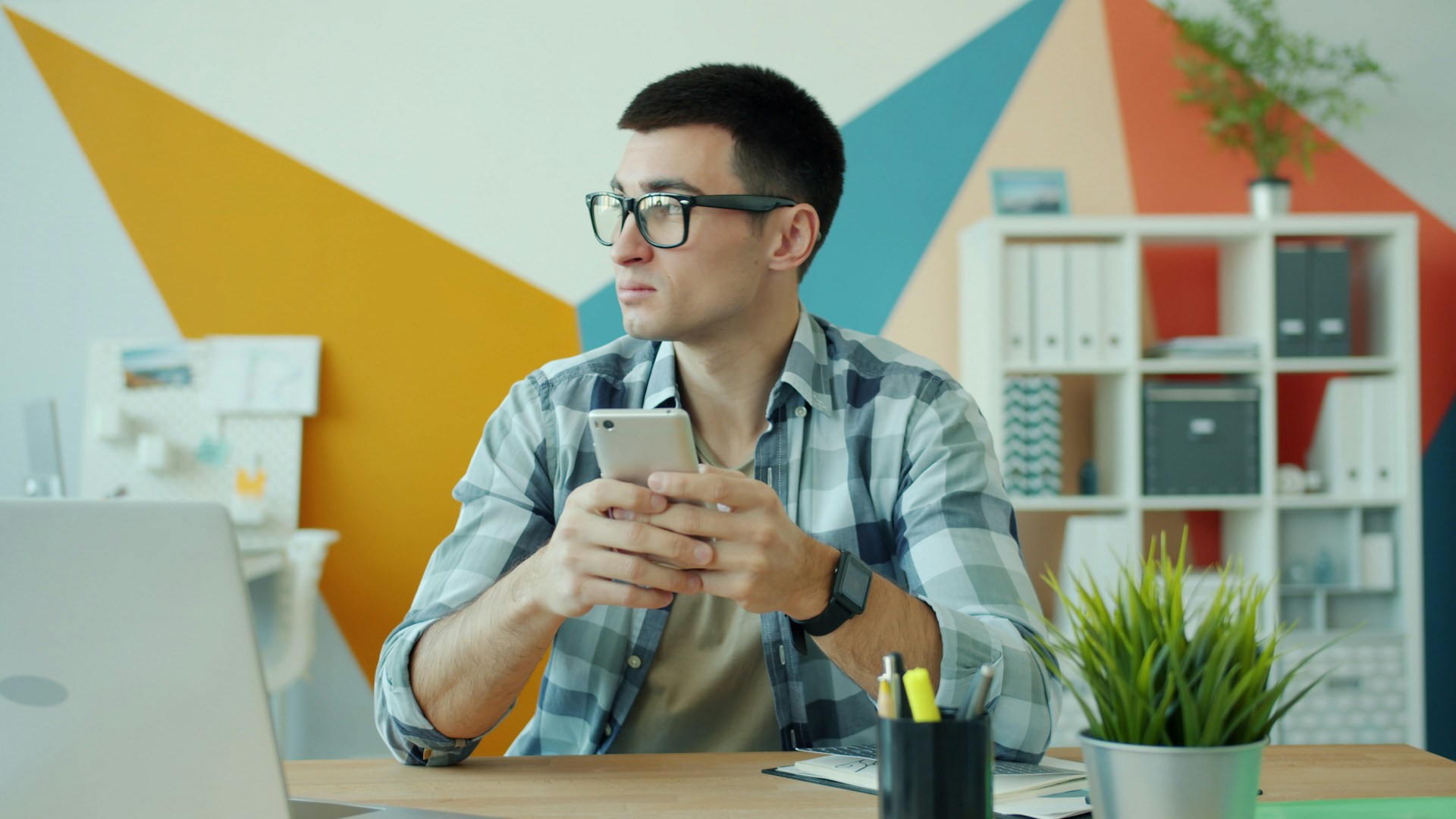 Man with glasses holding smartphone at desk